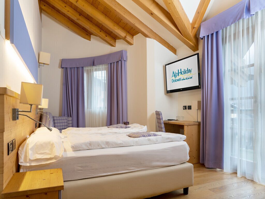 A hotel room with a bed, a desk, a TV, and a window with curtains.