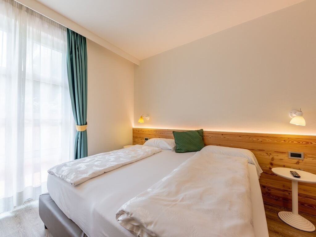 A hotel room with a bed, a bedside table with a lamp, and a view of the outside through sheer curtains.
