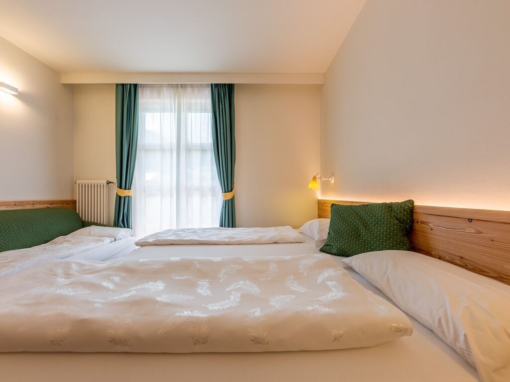 Quarto de hotel com uma cama grande, um radiador, uma janela com cortinas e uma luminária na parede.