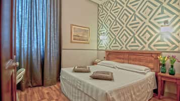 A hotel room with a bed, a nightstand, a lamp, a painting, and a patterned wall.