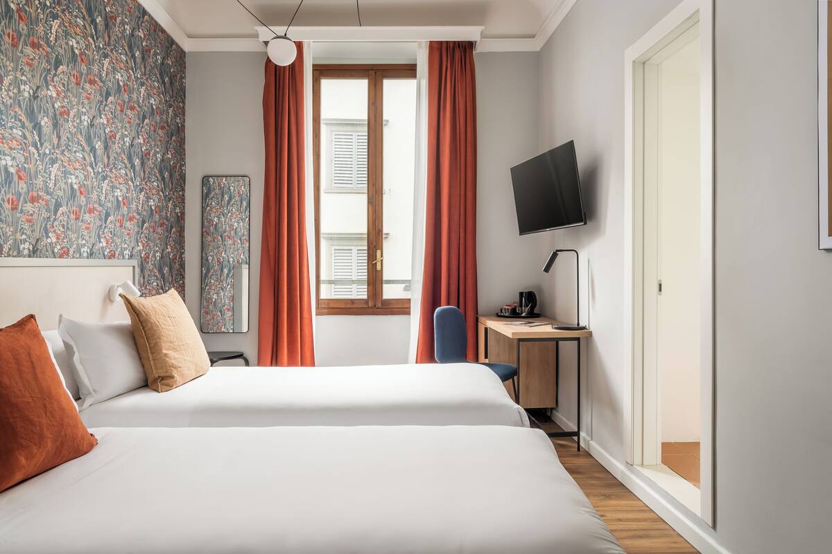 A hotel room with a large bed, a desk with a chair, a television, and a window with curtains.