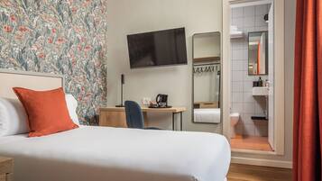 Hotelkamer met een bed, bureau, televisie, spiegel en een badkamer zichtbaar door een geopende deur.
