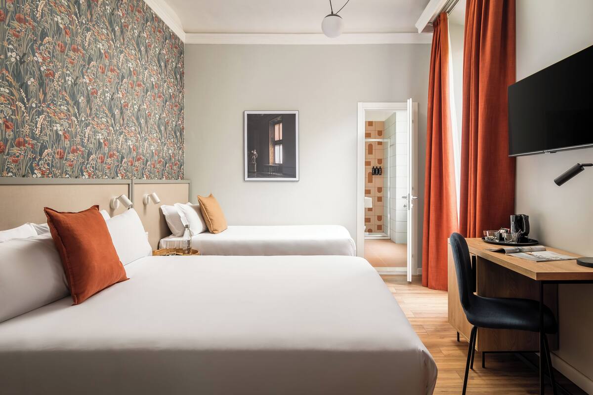 A hotel room with two beds, a desk, a chair, a TV, and a bathroom visible through an open door.