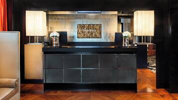 A reception desk with a modern design, featuring a large screen displaying the hotel name, two lamps, and a vase with flowers.