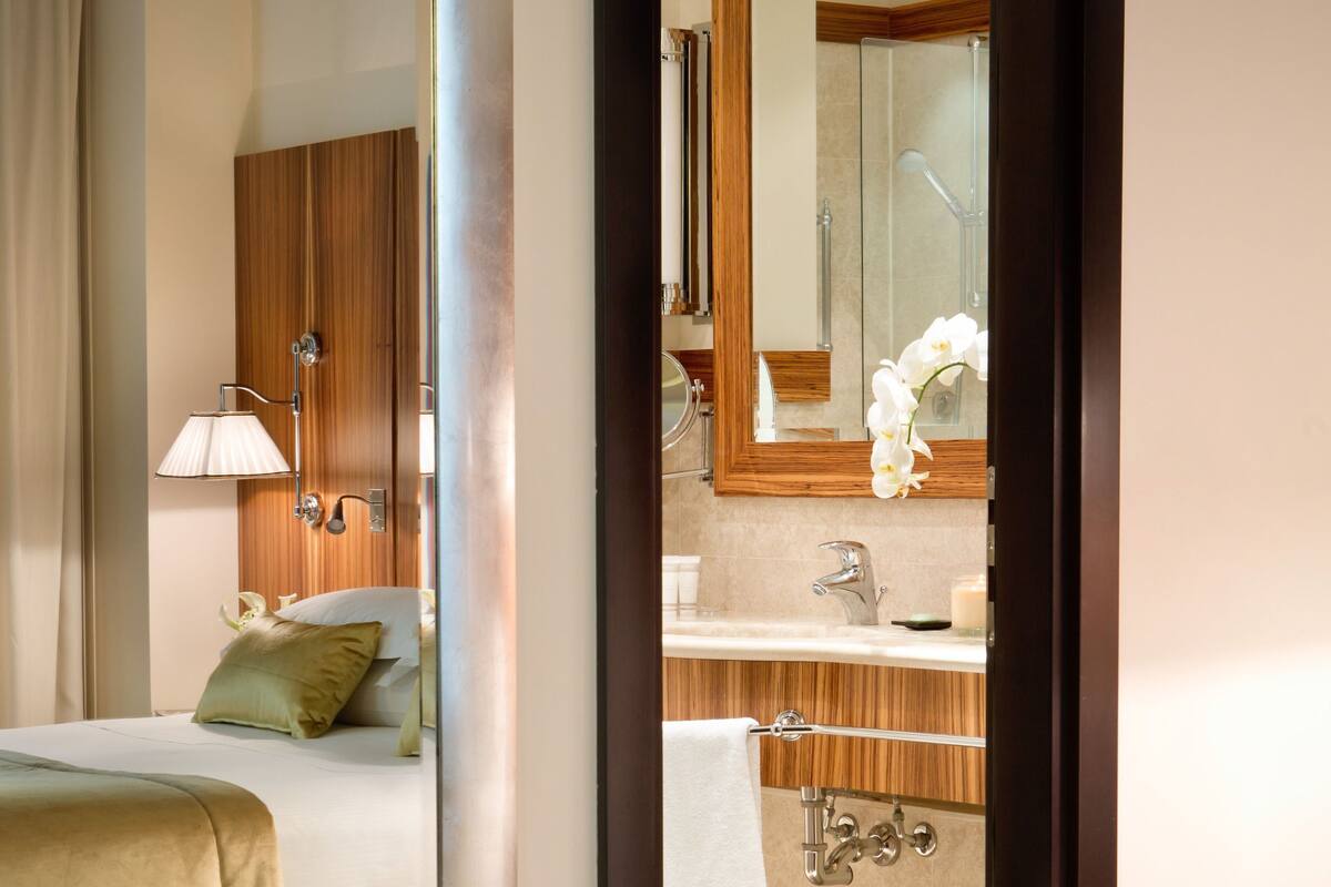 Een hotelkamer met een bed, een badkamer met een spiegel en een glazen tafel met een vaas.