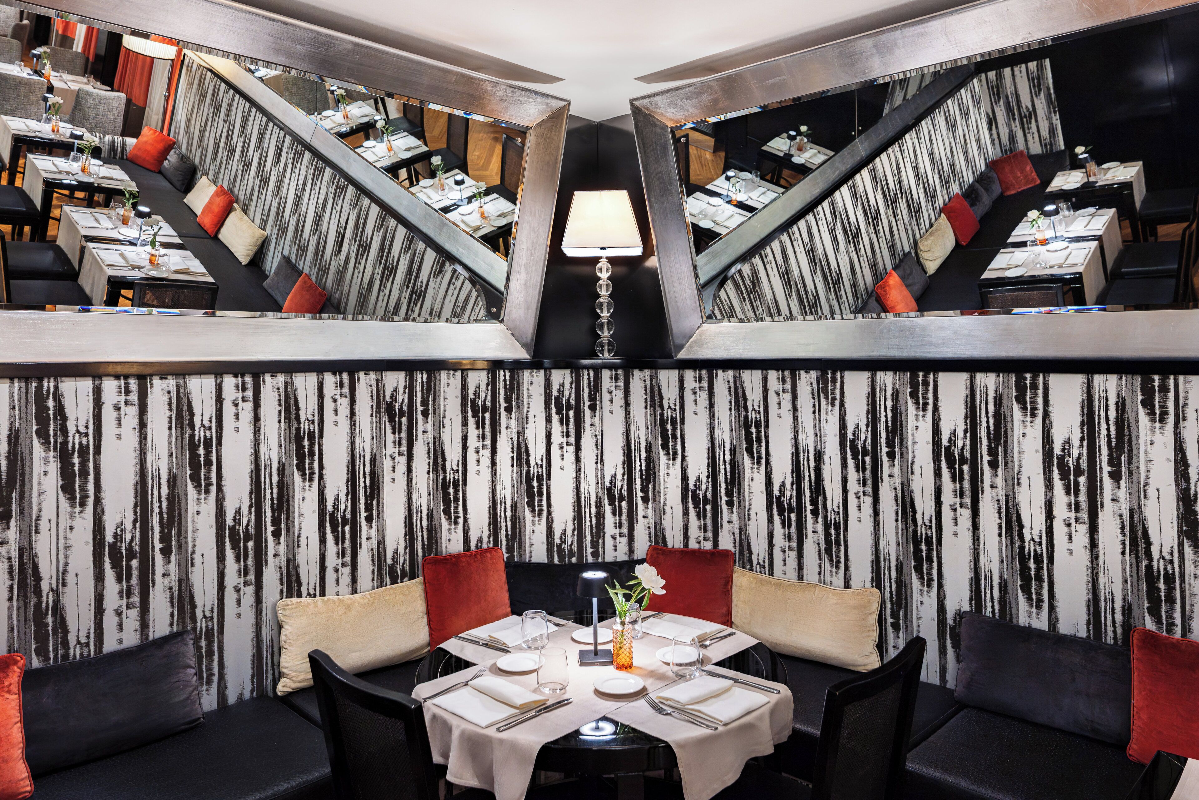 En restaurant med et rundt bord i midten, dækket til spisning, omgivet af polstrede stole i sort og rød.