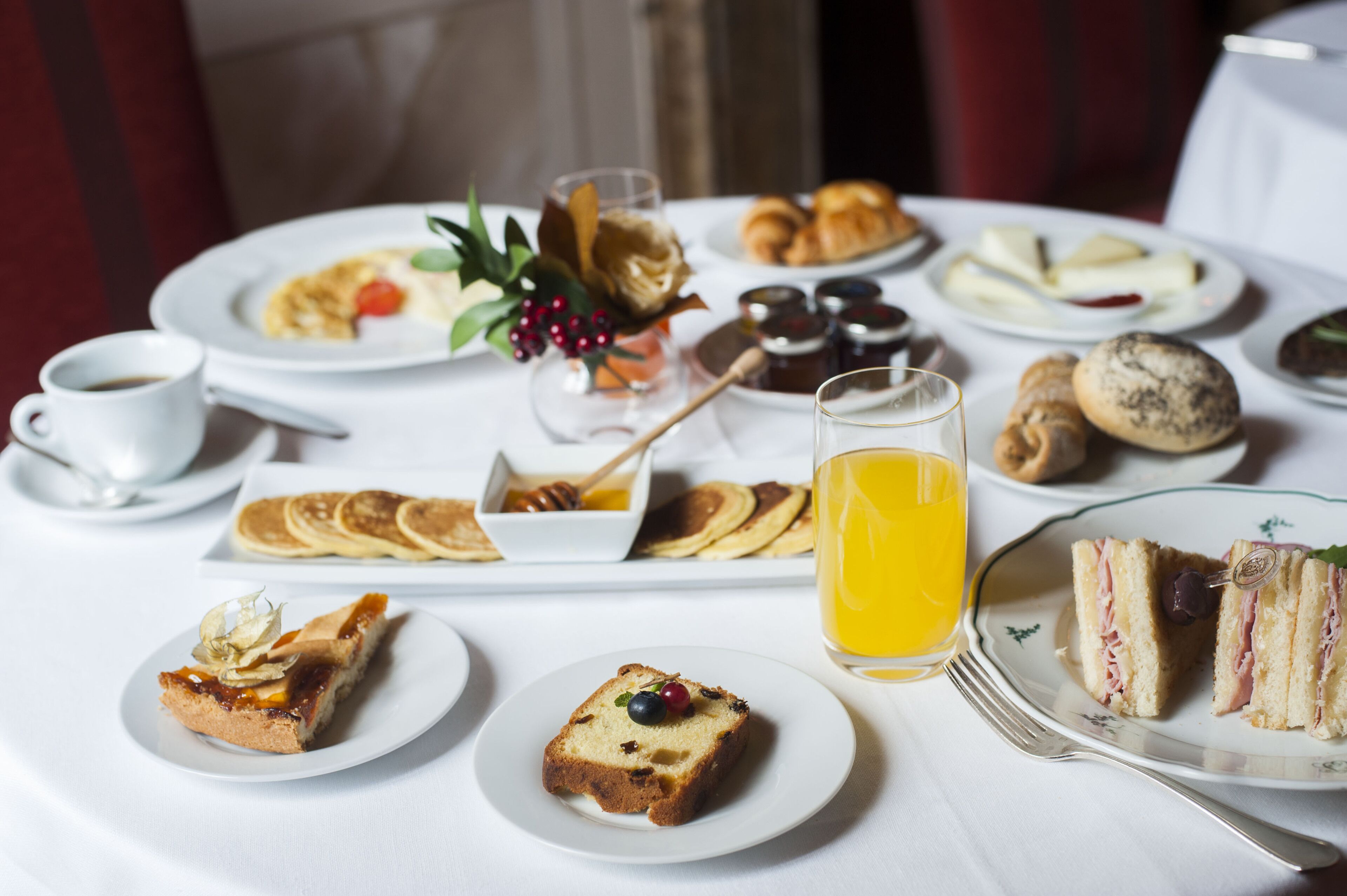 A breakfast setting with various dishes, including pancakes, croissants, and sandwiches, on a white table.
