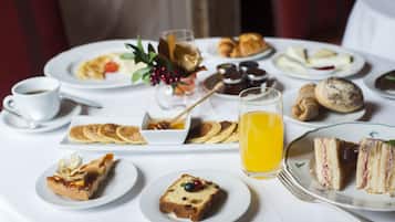 A breakfast setting with various dishes, including pancakes, croissants, and sandwiches, on a white table.