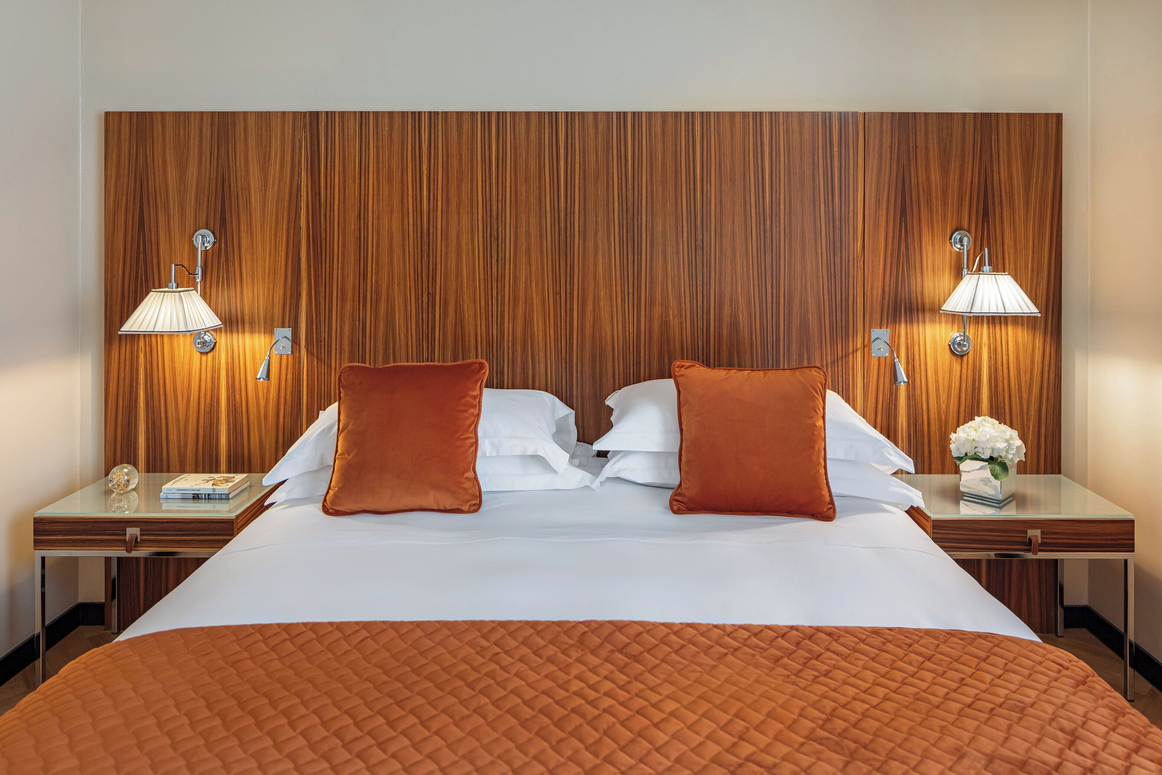 A hotel room with a large bed, two nightstands, a wooden headboard, and two wall-mounted lamps.