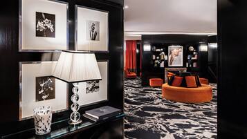 Un moderno vestíbulo de hotel con alfombra de diseño blanco y negro, un área de descanso circular naranja y obras de arte enmarcadas en las paredes.