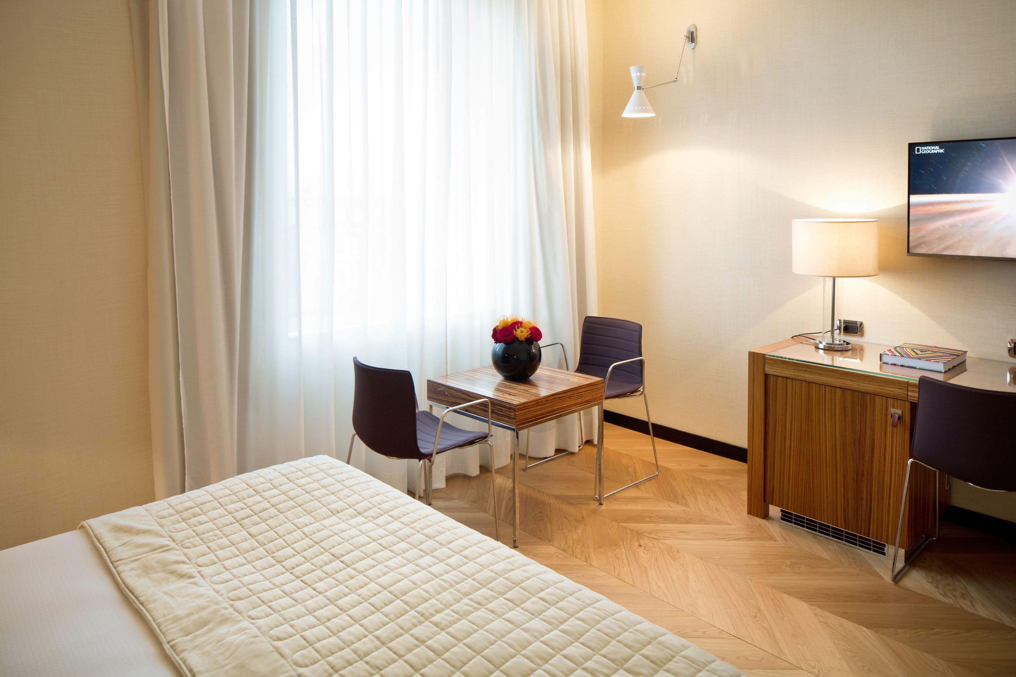 Et hotelværelse med en seng, et skrivebord med stol, et fjernsyn og en lampe.