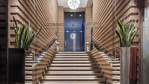 Una escalera moderna con escalones de madera y barandillas de vidrio, que conduce a una puerta con un aplique decorativo encima.