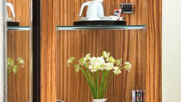 Uma parede de madeira com um vaso de flores brancas, uma chaleira e livros nas prateleiras.
