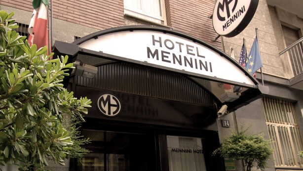 Außenansicht des Hotel Mennini mit auffälliger Beschilderung, einer Überwachungskamera und einem Blumentopf im Vorbereich.