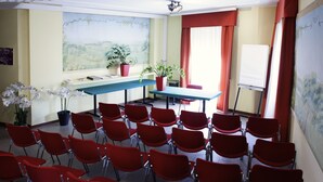 Ein Konferenzraum mit roten Stühlen, einem Tisch, Topfpflanzen und einer Whiteboard.