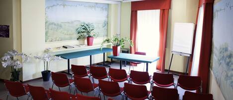 Une salle de conférence avec des chaises rouges, une table, des plantes en pot et un tableau blanc.