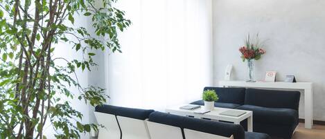 Una sala de estar moderna con un sofá blanco, un sofá negro, una mesa de centro blanca y una planta en maceta.