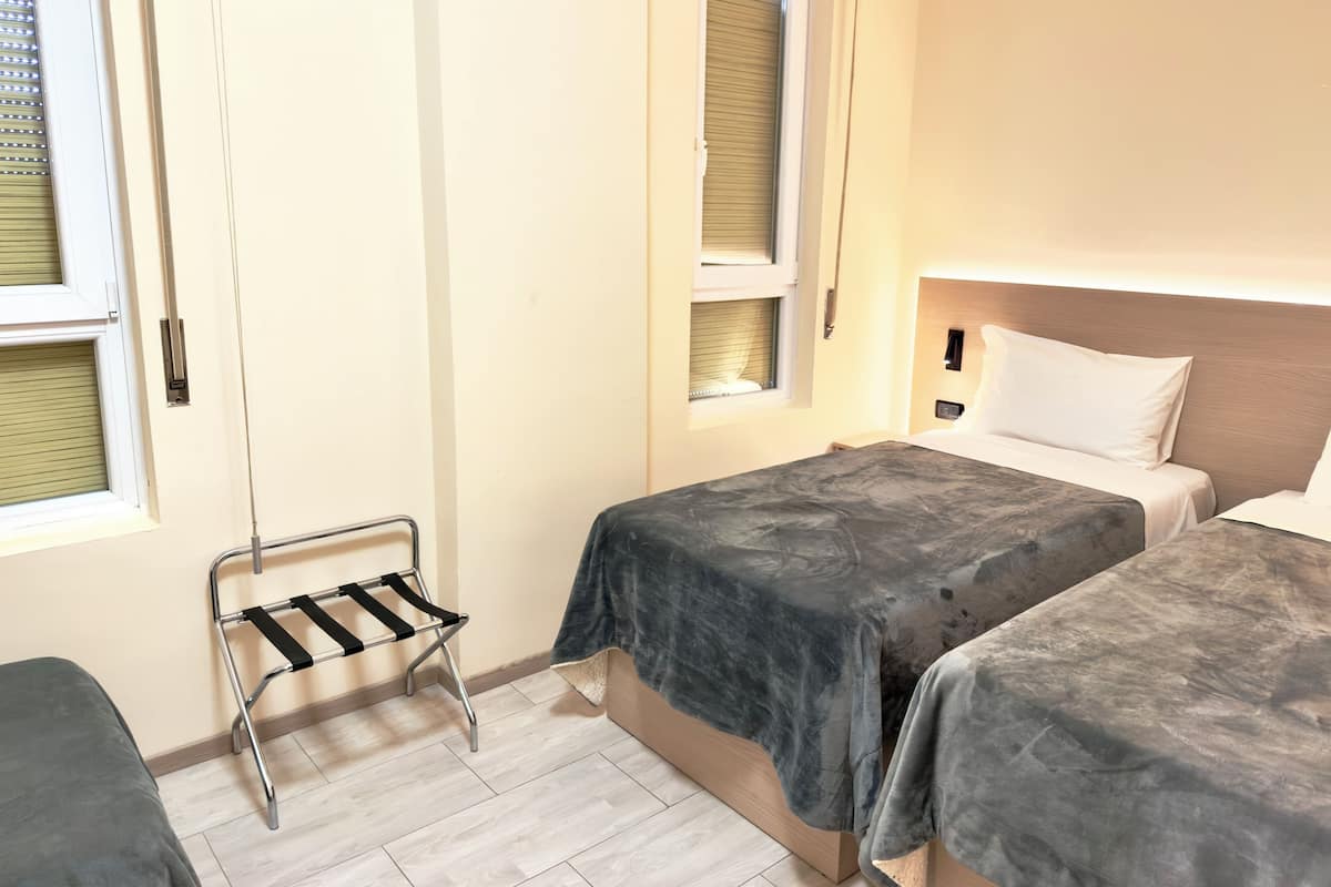 Ein Hotelzimmer mit zwei Betten, einem kleinen Tisch, einem Stuhl und einem Fenster mit Jalousien.