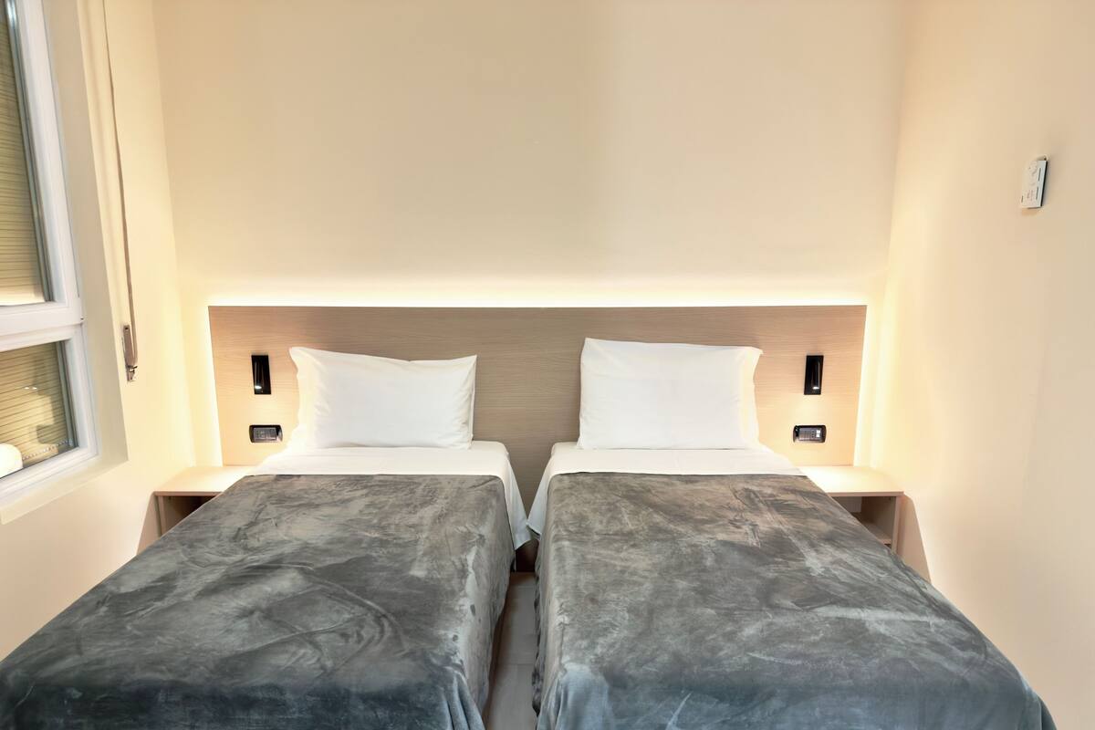 Ein Doppelzimmer mit zwei Einzelbetten, Nachttischen und einem Fenster.