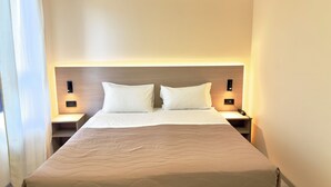 Quarto de hotel com uma cama grande, duas mesas de cabeceira e cabeceira com iluminação embutida.