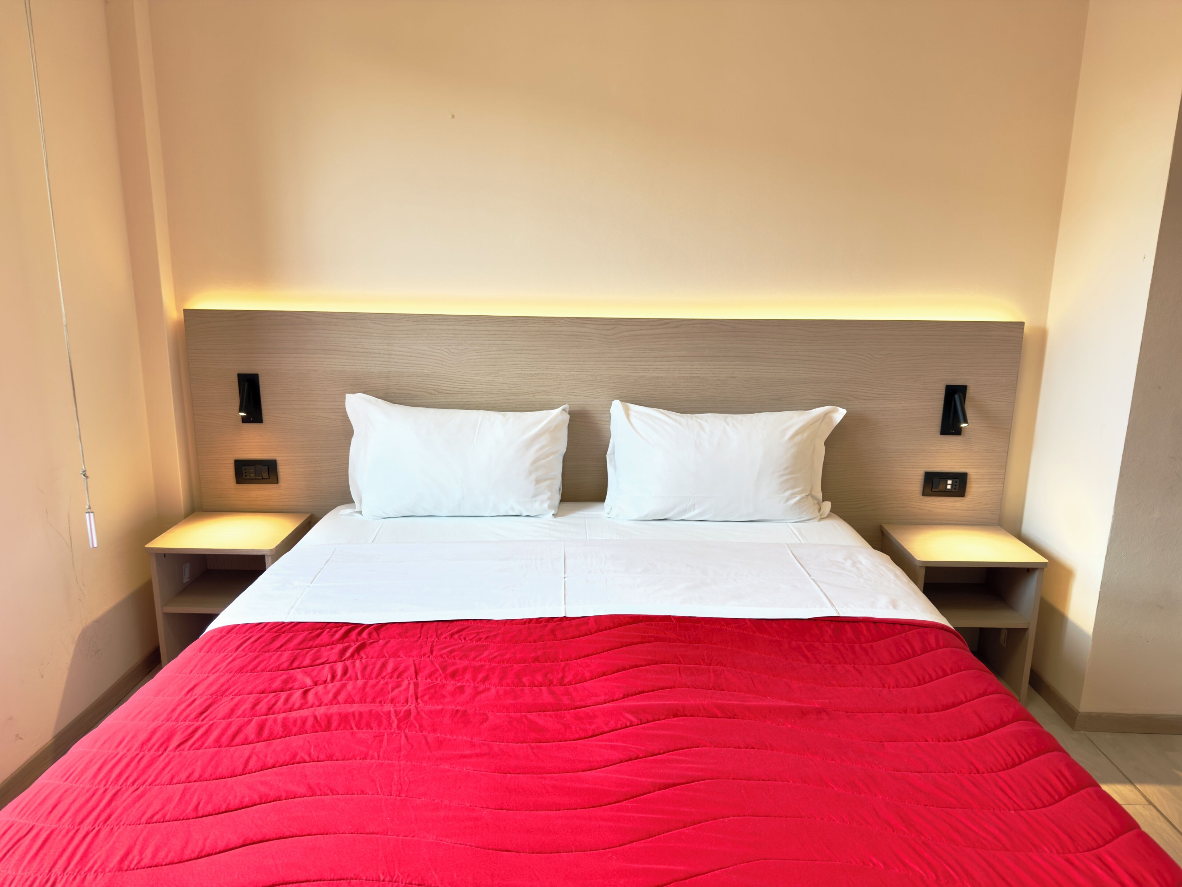 A hotel room with a bed, two bedside tables, and a headboard with wall-mounted lights.