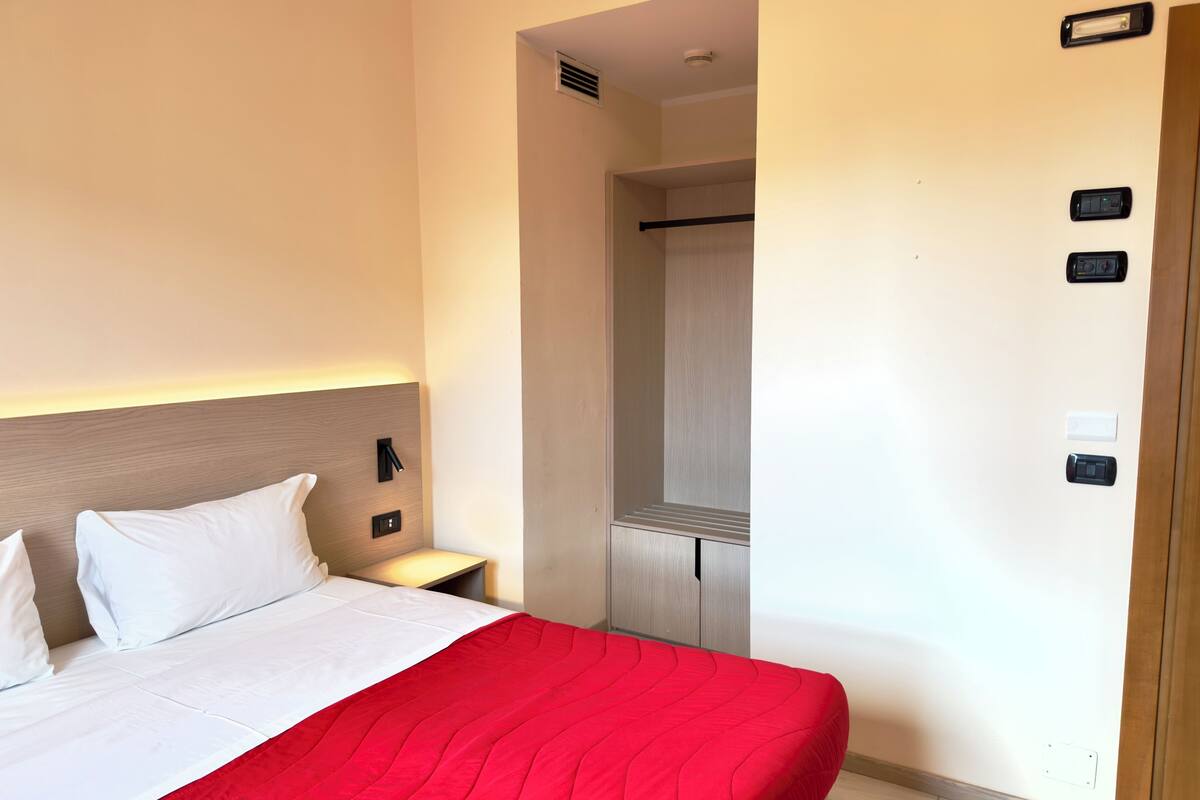 Ein Hotelzimmer mit Bett, Schrank, Nachttisch und Wandleuchte.
