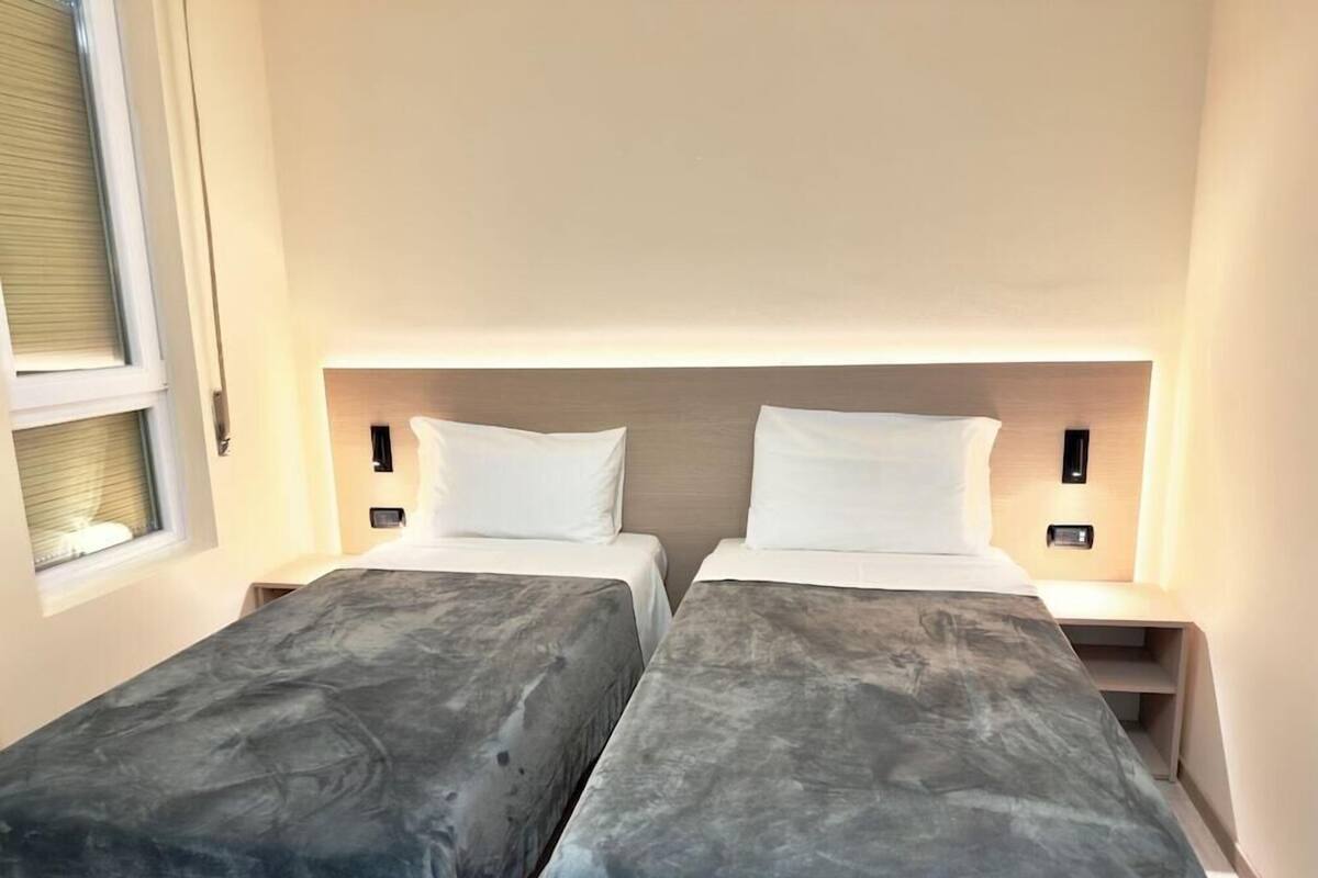 Ein Hotelzimmer mit zwei Einzelbetten, einem Fenster mit Jalousien und Nachttischen mit Lampen.