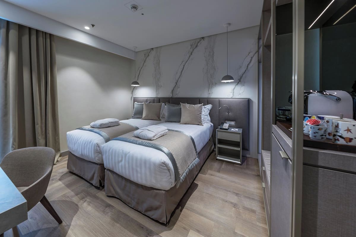 A modern hotel room with a large bed, bedside tables, a desk, and a wardrobe.