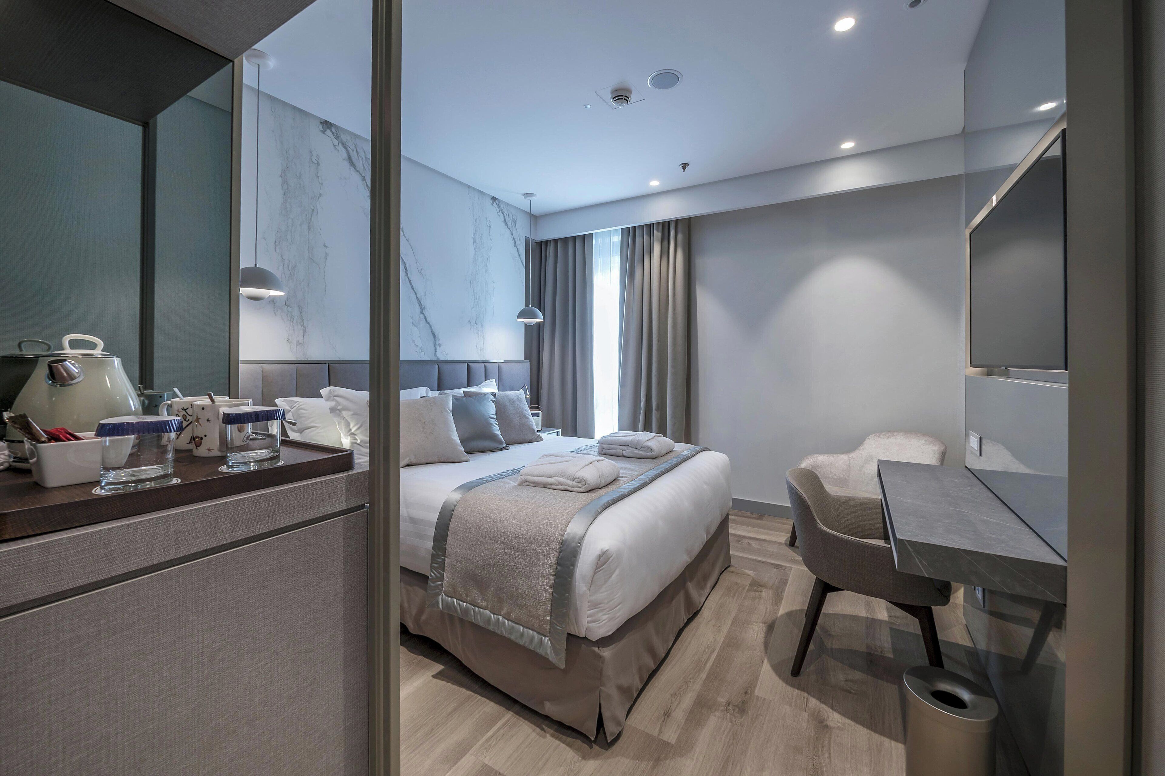 A modern hotel room with a large bed, a desk, a chair, a TV, and a bathroom.