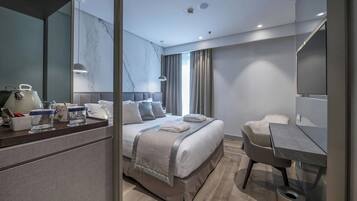A modern hotel room with a large bed, a desk, a chair, a TV, and a bathroom.