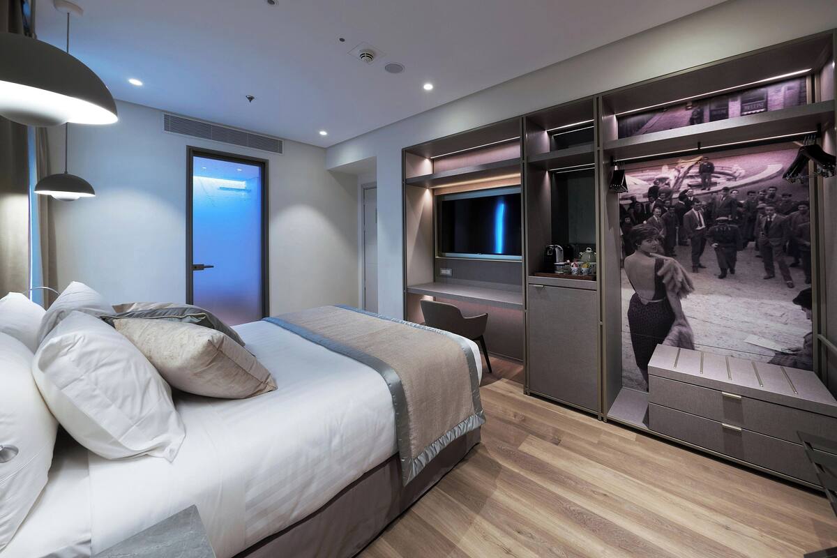 A modern bedroom with a bed, bedside tables, a desk, and a large mirror.