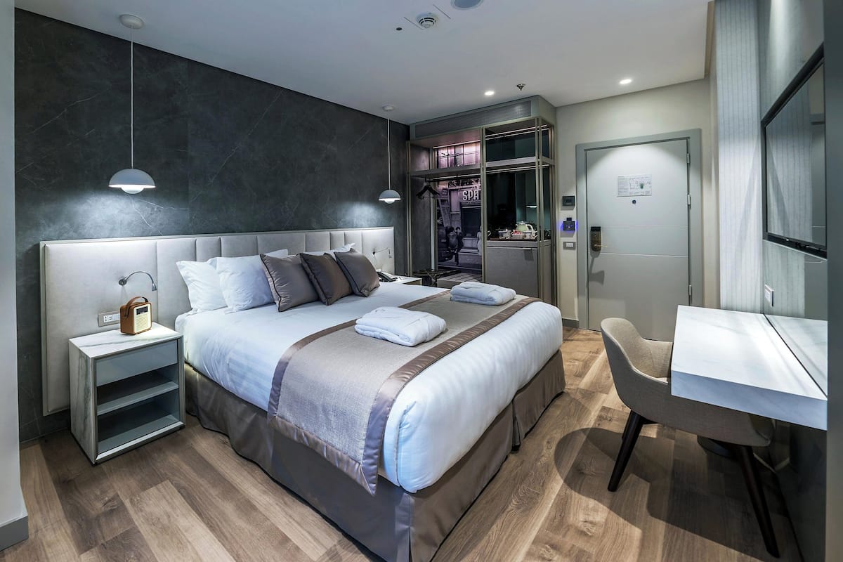 A modern hotel room with a large bed, bedside tables, a desk, and a chair.