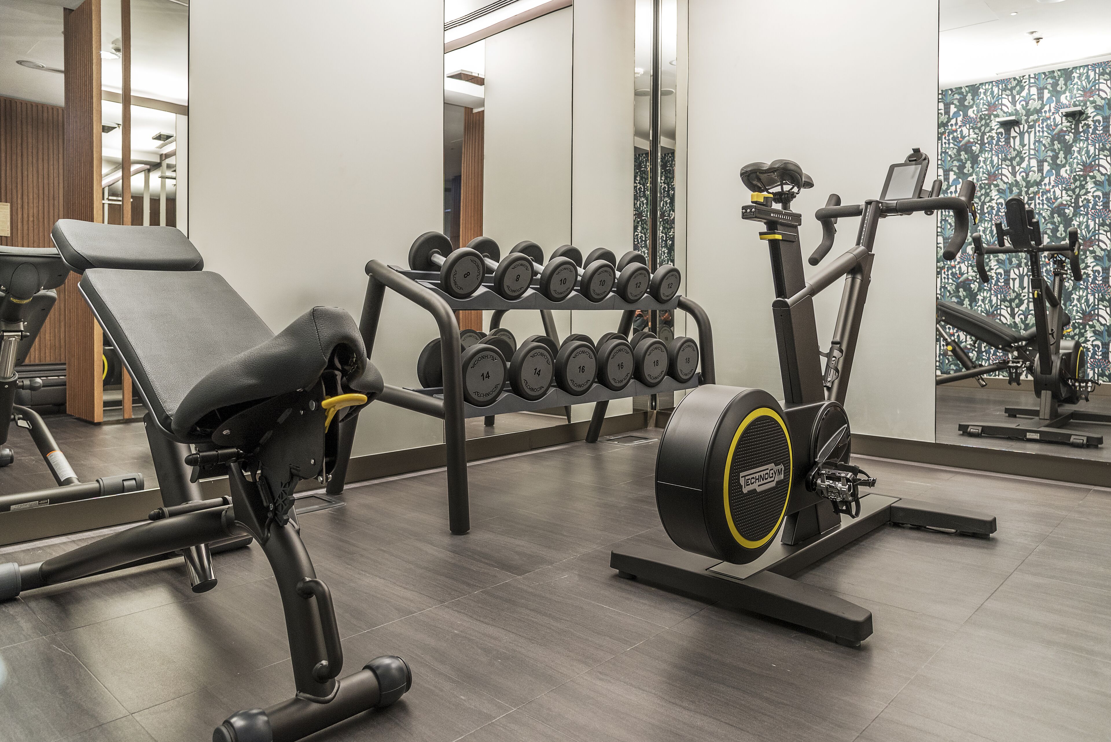 Ein Fitnessraum mit Trainingsgeräten, darunter eine Bank, Kurzhanteln und ein Crosstrainer.