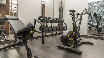 Ein Fitnessraum mit Trainingsgeräten, darunter eine Bank, Kurzhanteln und ein Crosstrainer.