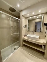 A modern bathroom with a glass-enclosed shower, a large mirror, and a white sink.
