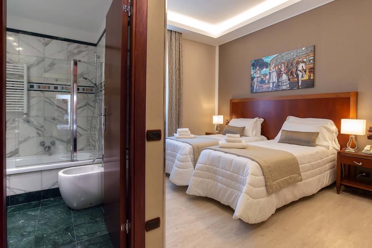 A hotel room with a shower, two beds, a painting, and a wooden headboard.
