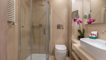 A modern bathroom with a glass-enclosed shower, a white toilet, a large sink, and a mirror.