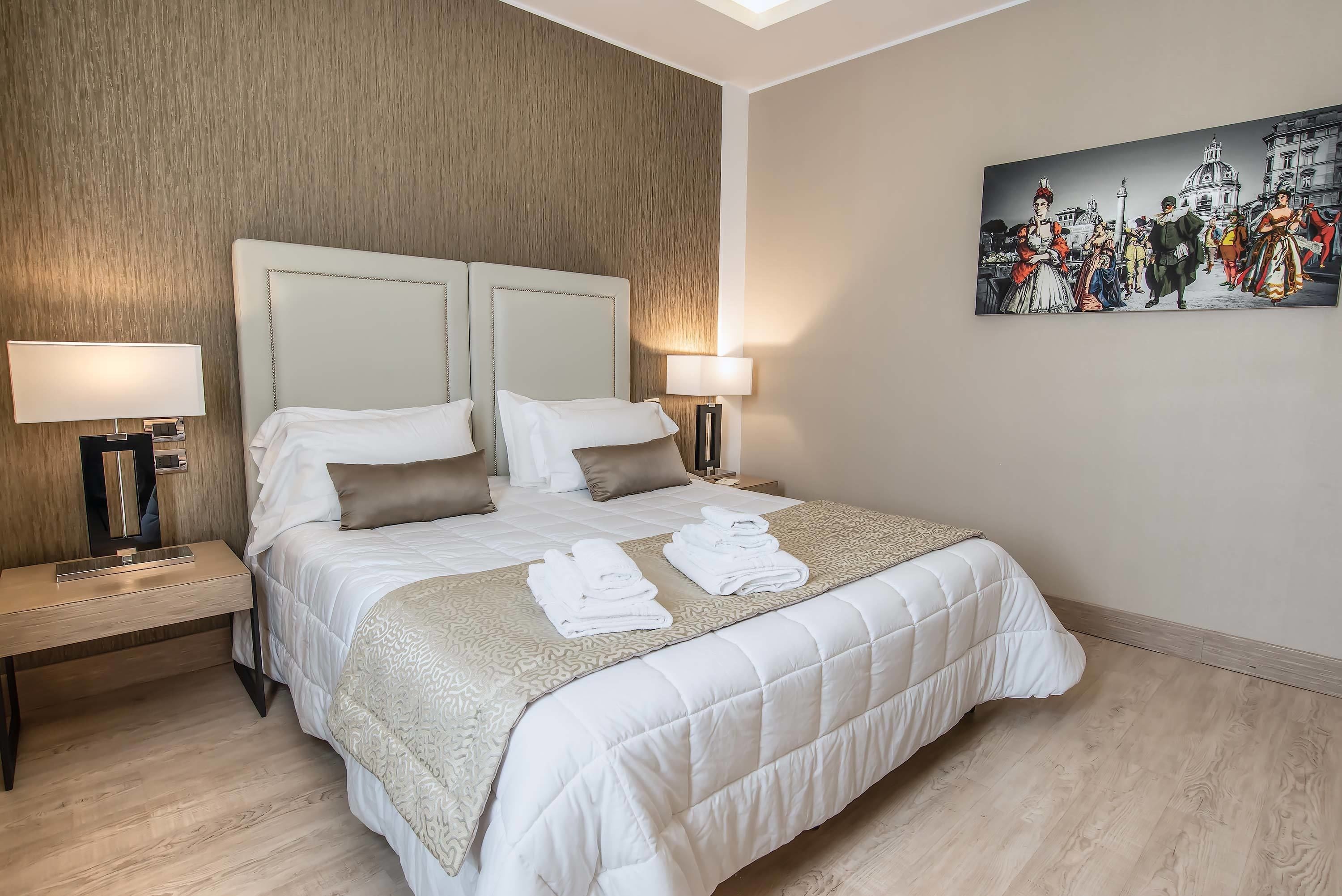 A hotel room with a large bed, two bedside tables with lamps, a painting on the wall, and a wooden floor.