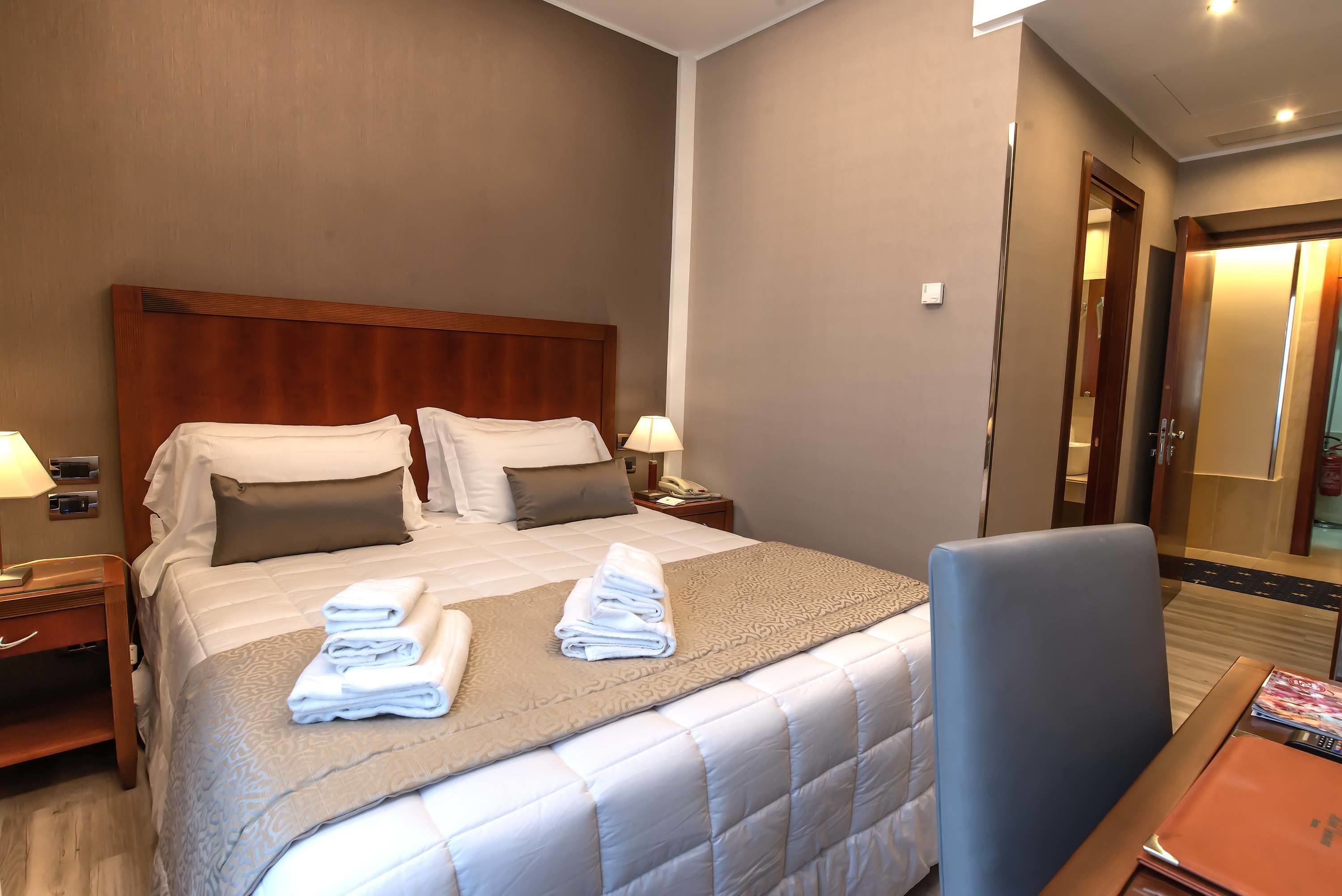 A hotel room with a large bed, two bedside tables, a chair, and a desk.