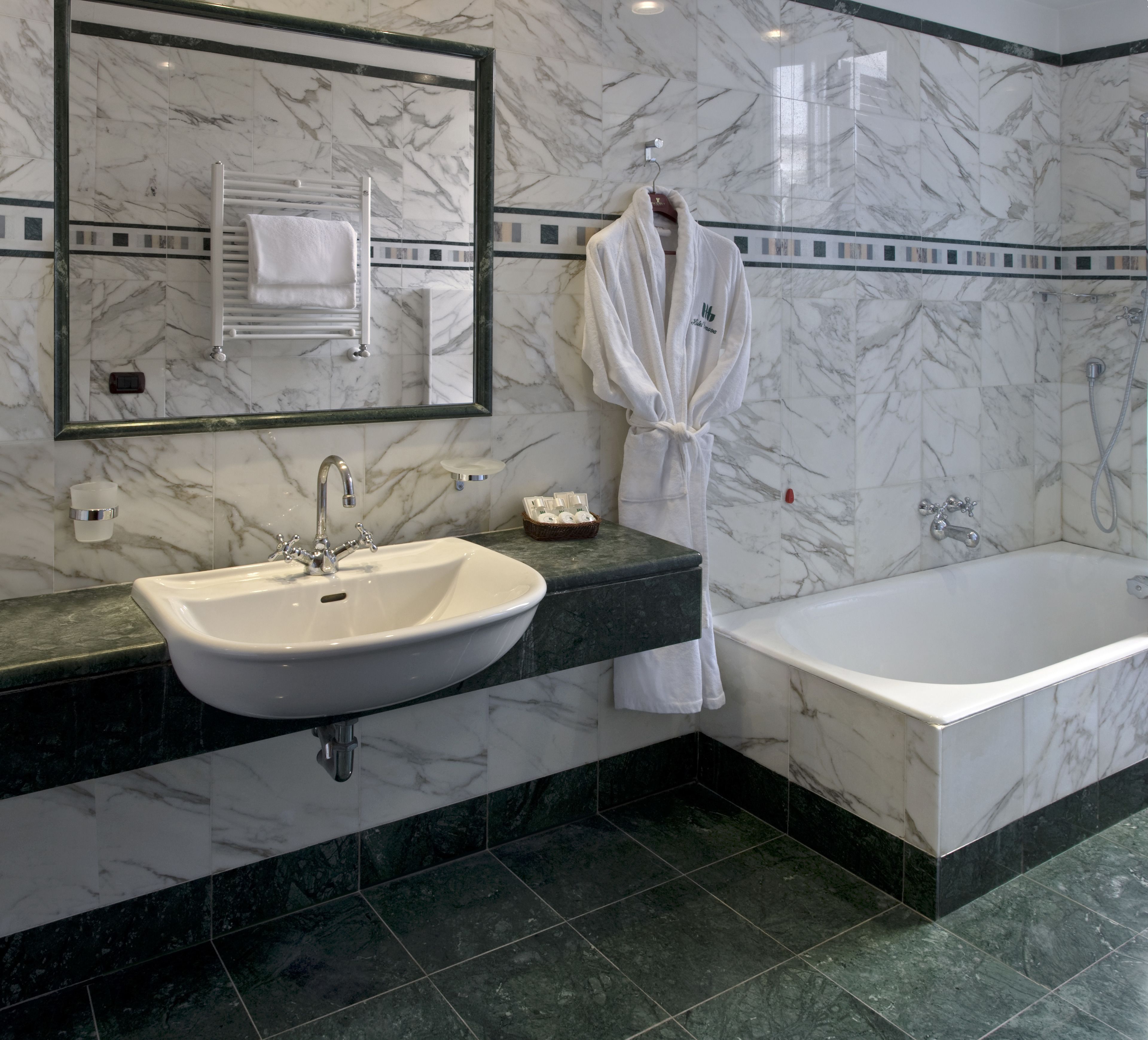 A bathroom with a marble sink, a bathtub, and a robe hanging on a rack.