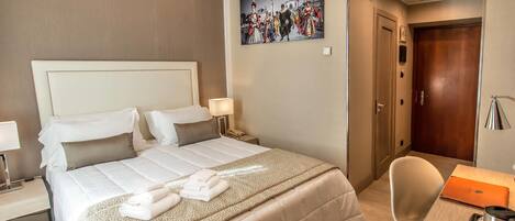 A hotel room with a large bed, a desk with a laptop, a chair, and a painting on the wall.