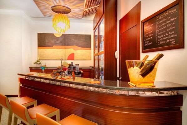 Zona de bar con mostrador de madera, taburetes y una pizarra con la carta de bebidas.