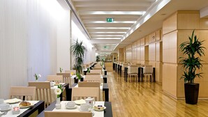 Un grand espace dédié à la salle à manger, avec de longues tables, des chaises et des plantes en pot.