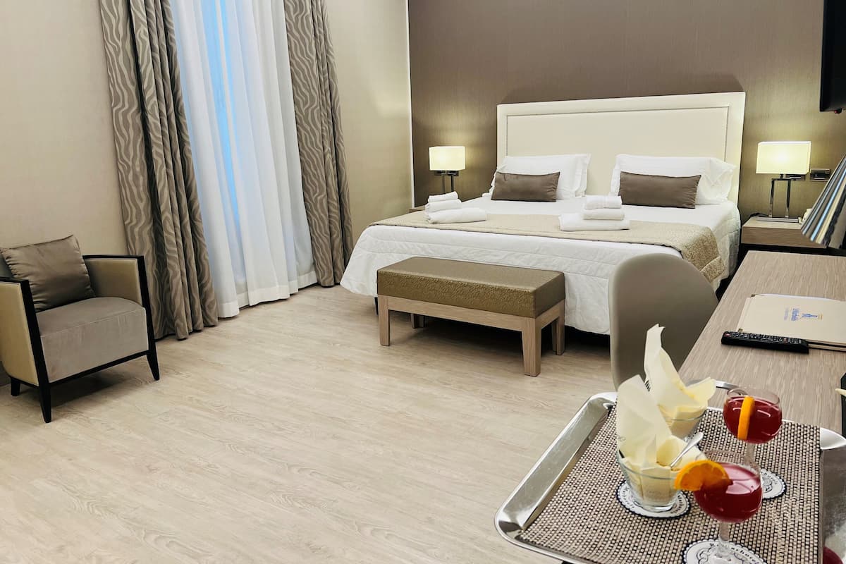 A hotel room with a large bed, bedside tables, a chair, a bench, and a tray with drinks.