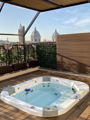 A hot tub on a wooden deck with a view of historic buildings in the background. - Hotel Genova (Rome)