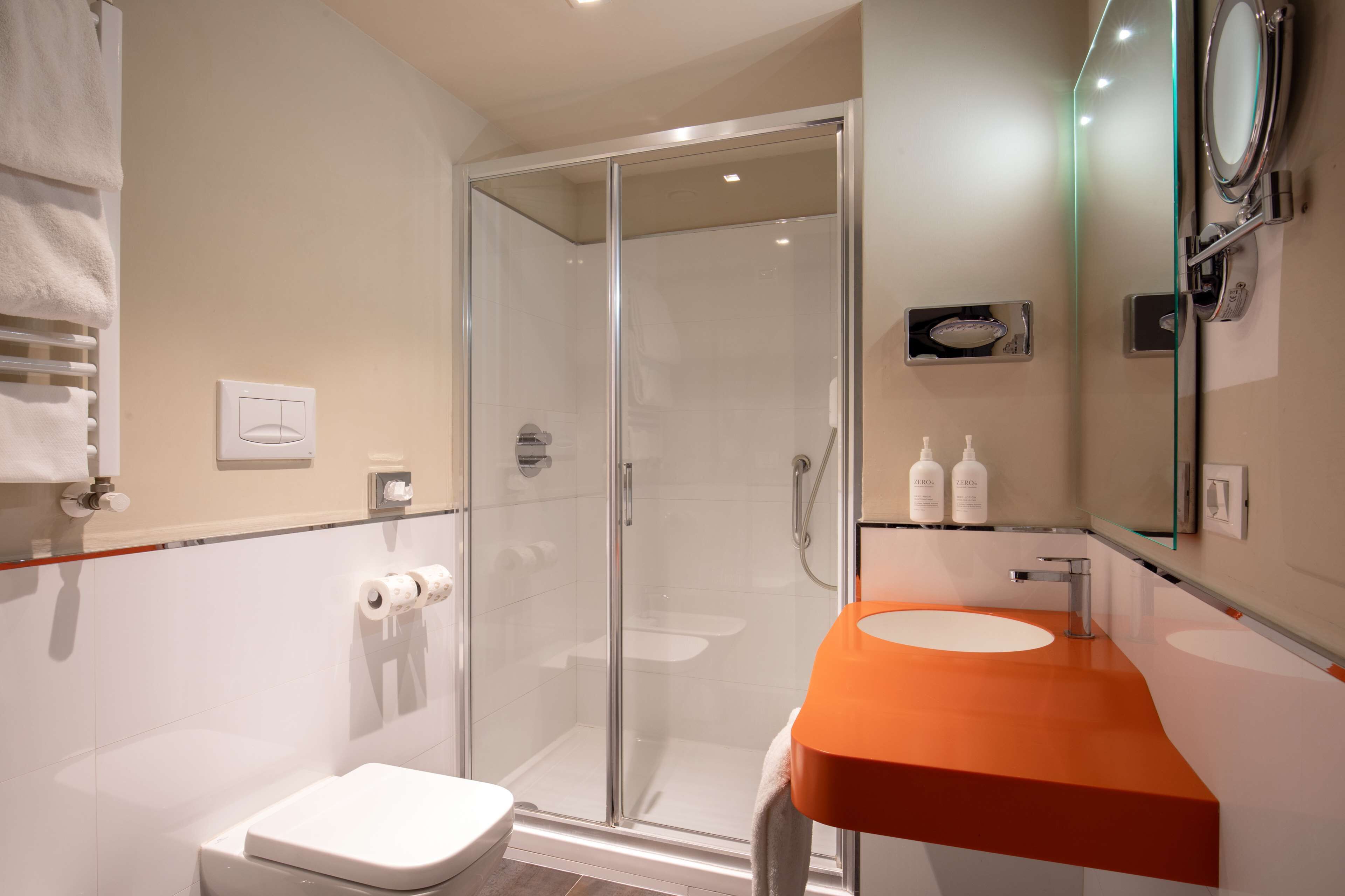 Een moderne badkamer met een douche in een glazen cabine, een wit toilet en een oranje wastafel.