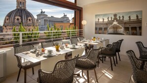 A dining area with a view of a historic building, wicker chairs, and a table set with plates and cups. - Cosmopolita Rome Colosseum, Tapestry Collection by Hilton (Rome)