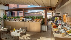 A breakfast buffet with a variety of food items, a seating area with chairs, and a view of the city through large windows. - Cosmopolita Rome Colosseum, Tapestry Collection by Hilton (Rome)