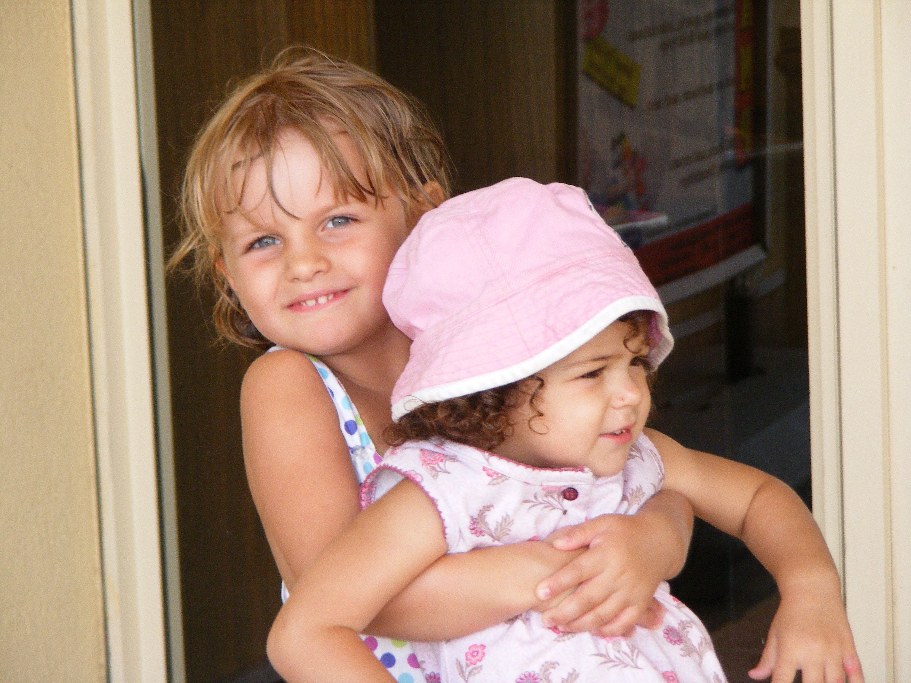 Two children hugging, one in a pink hat and the other in a polka dot dress.