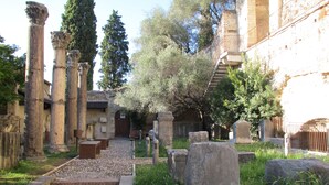 Ruinas antiguas con columnas, una escalera de piedra y un edificio con balcón.